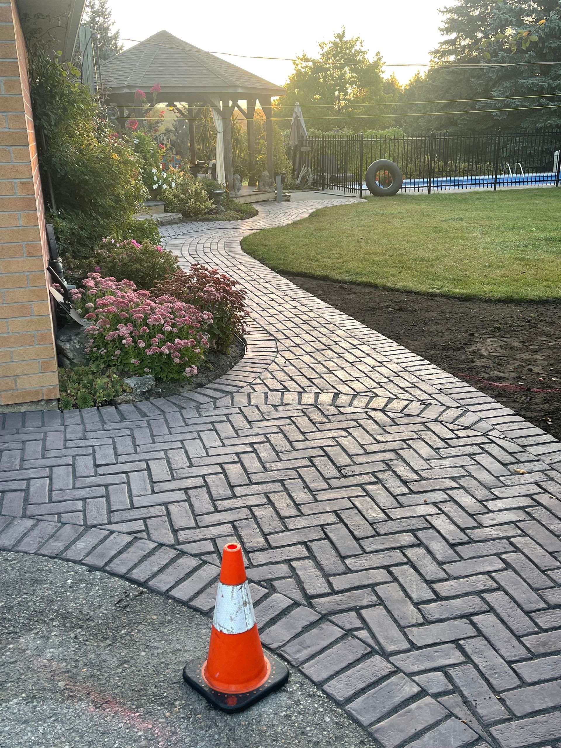A brick walkway with a traffic cone on the side of it.