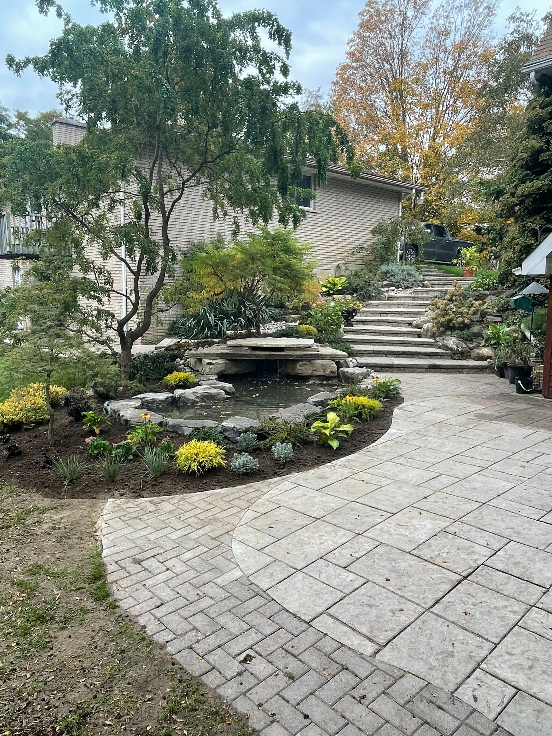 A brick walkway leading up to a house with a pond and stairs.