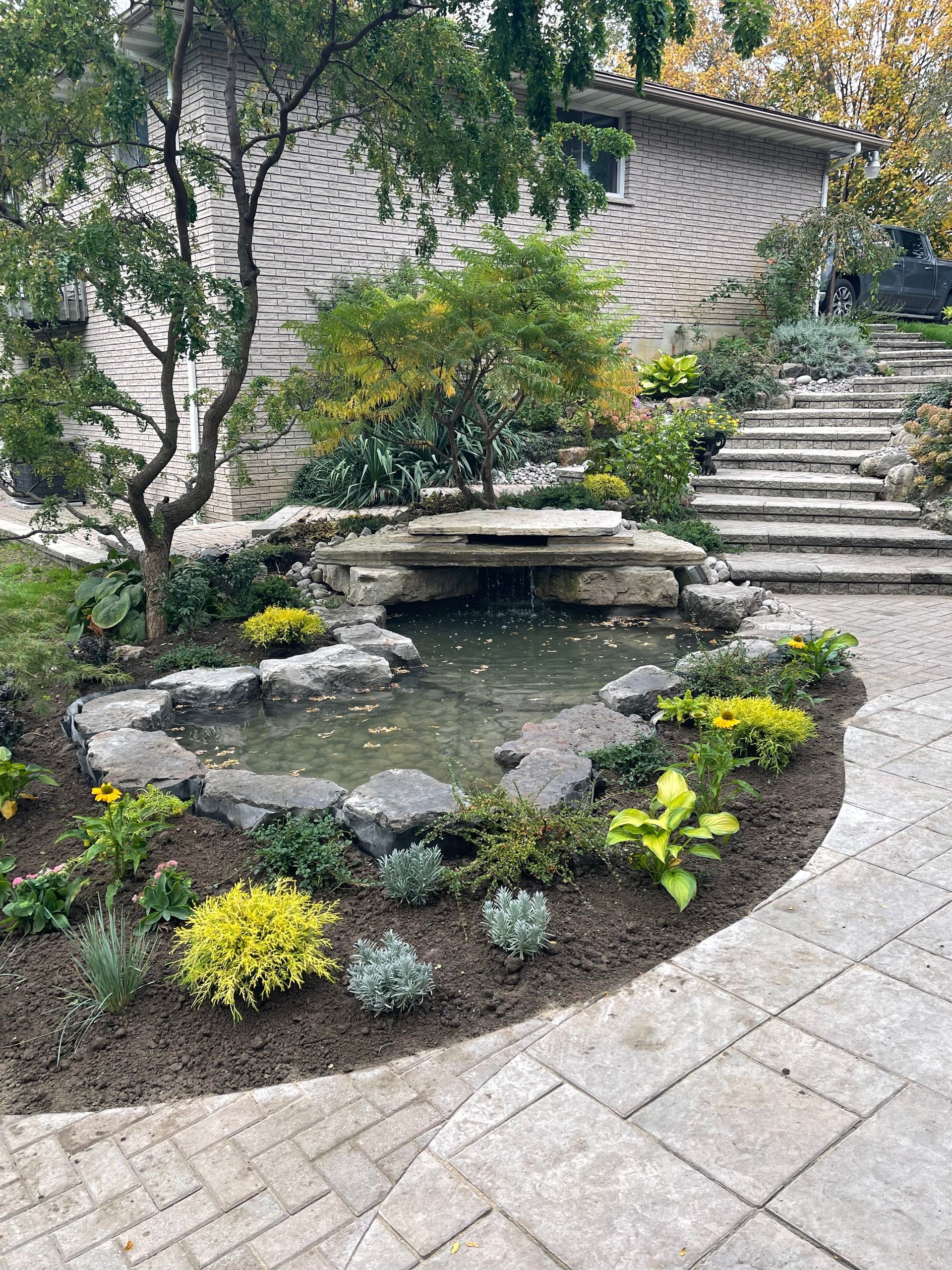 A garden with a pond and stairs in front of a house.