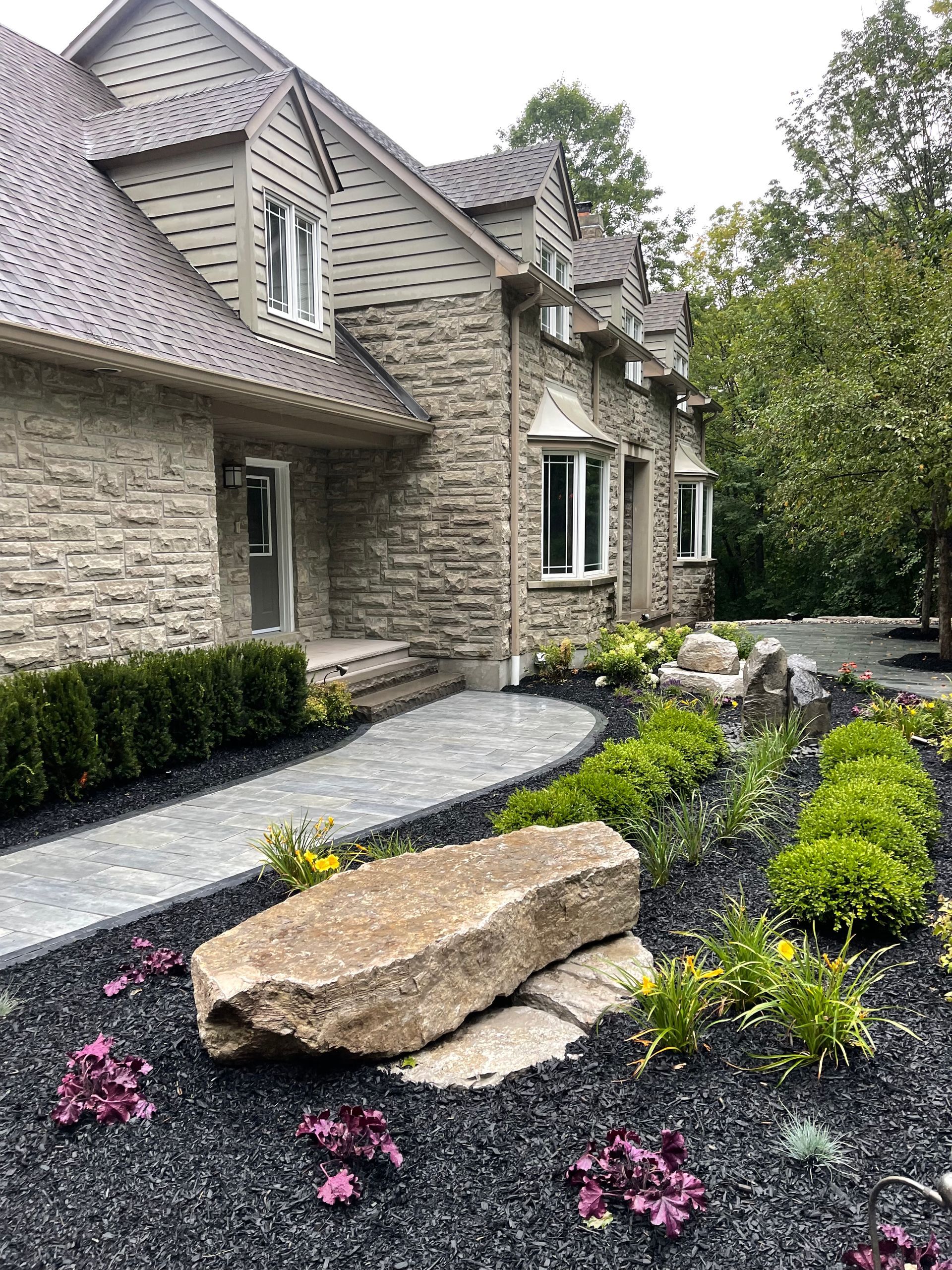 A large brick house with a walkway leading to it and a large rock in front of it.