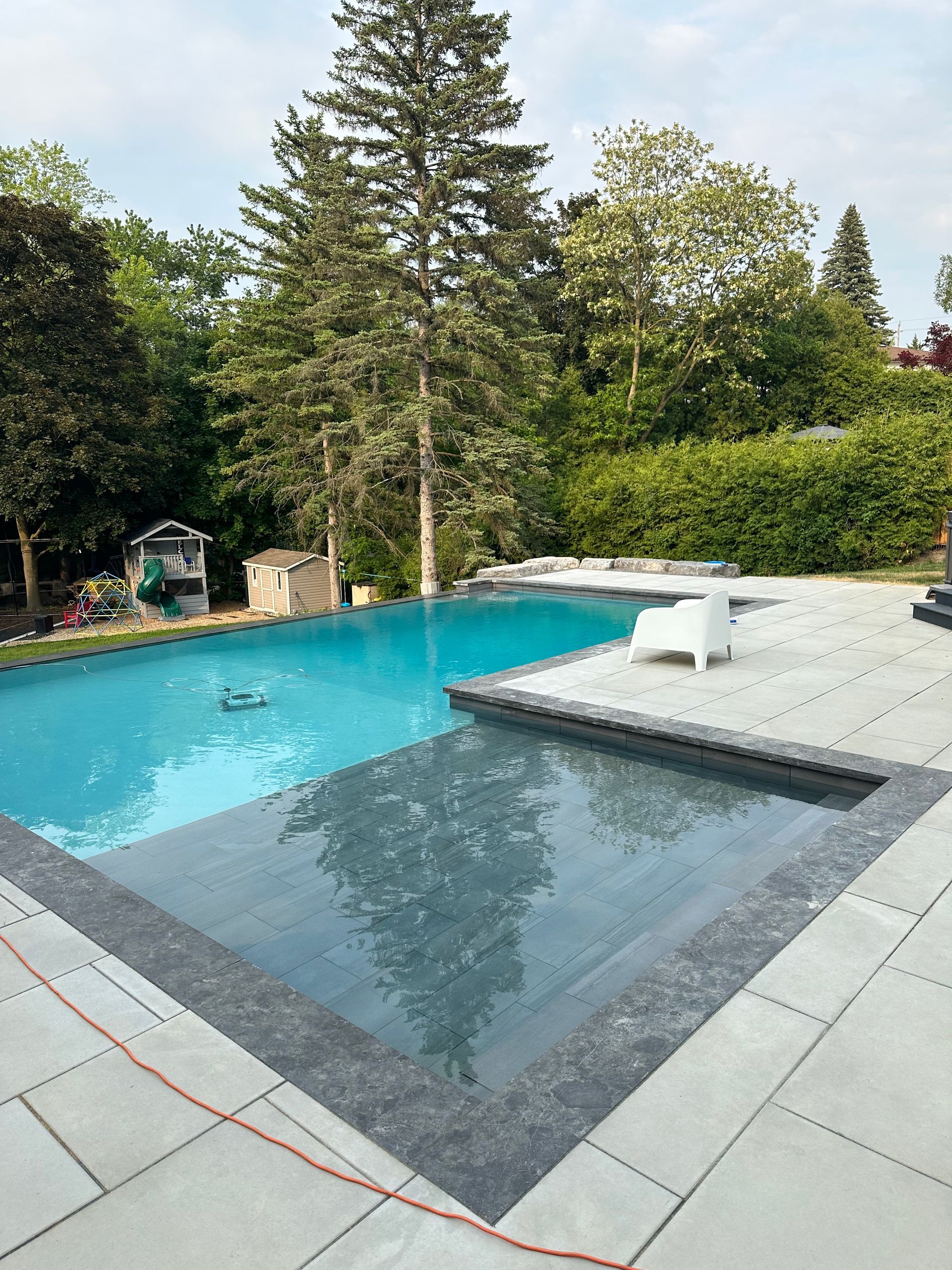 A large swimming pool is surrounded by trees and a patio.
