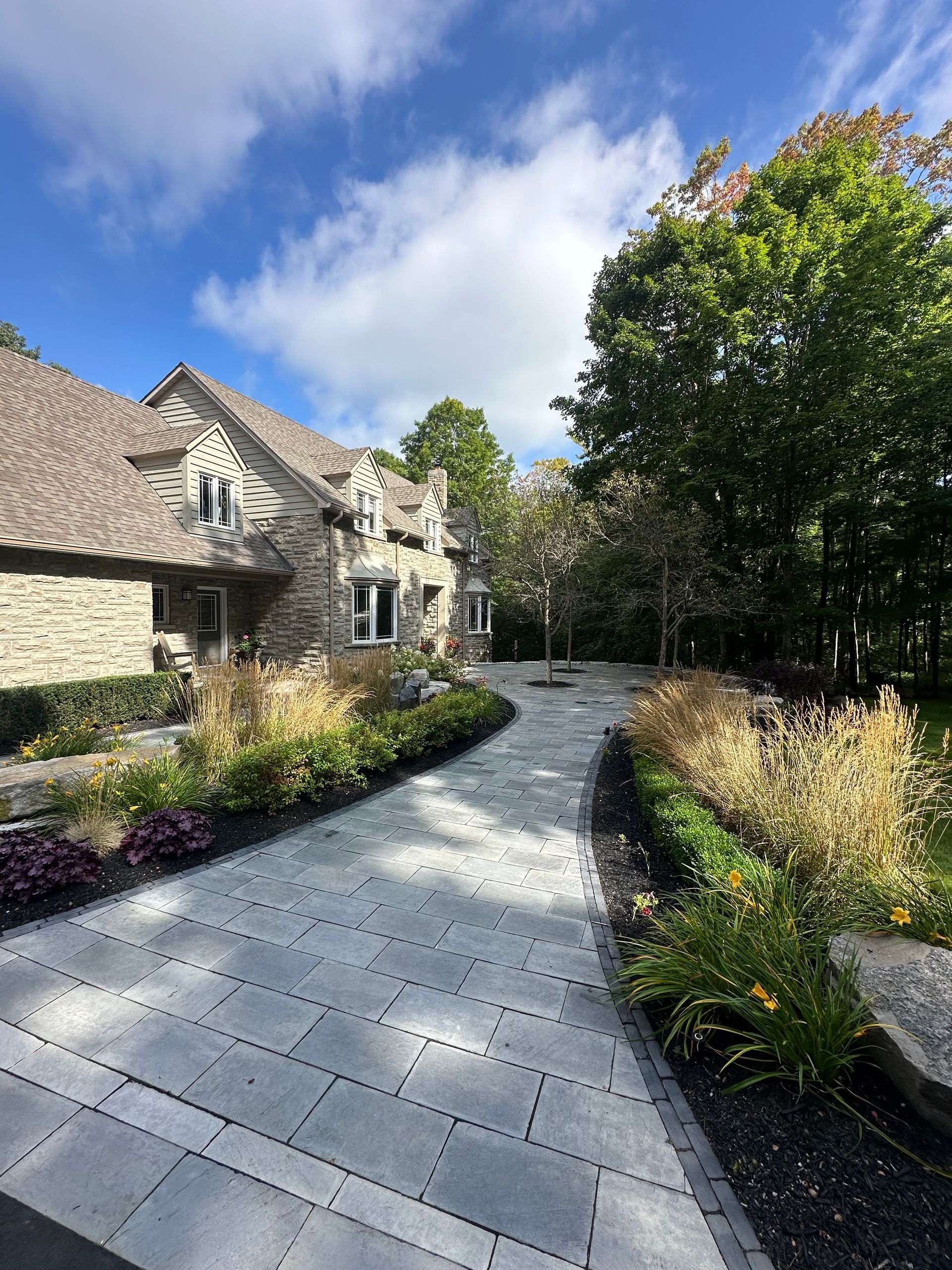 A stone driveway leading to a large house with trees on both sides.