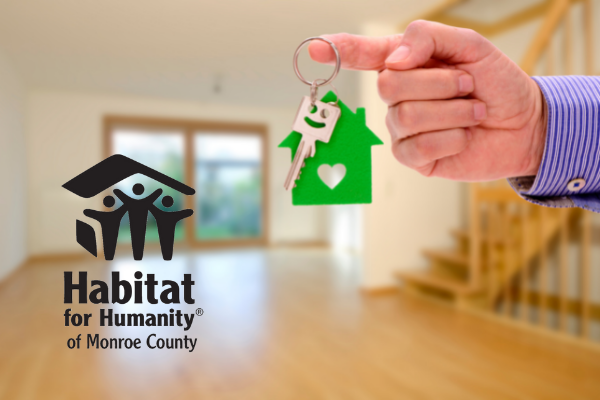 A person is holding a key in front of a habitat for humanity logo