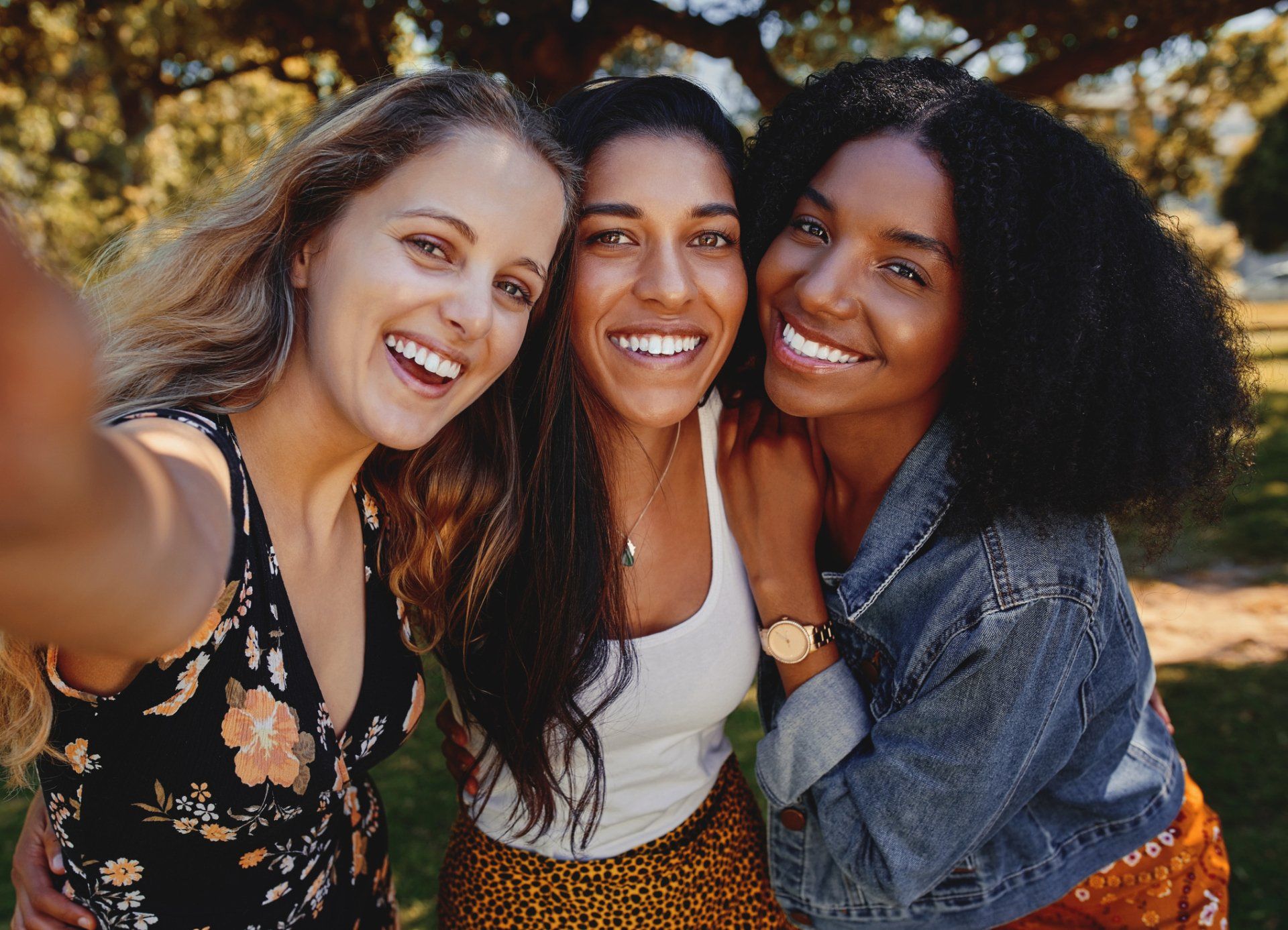 Three women are taking a selfie together in a park.