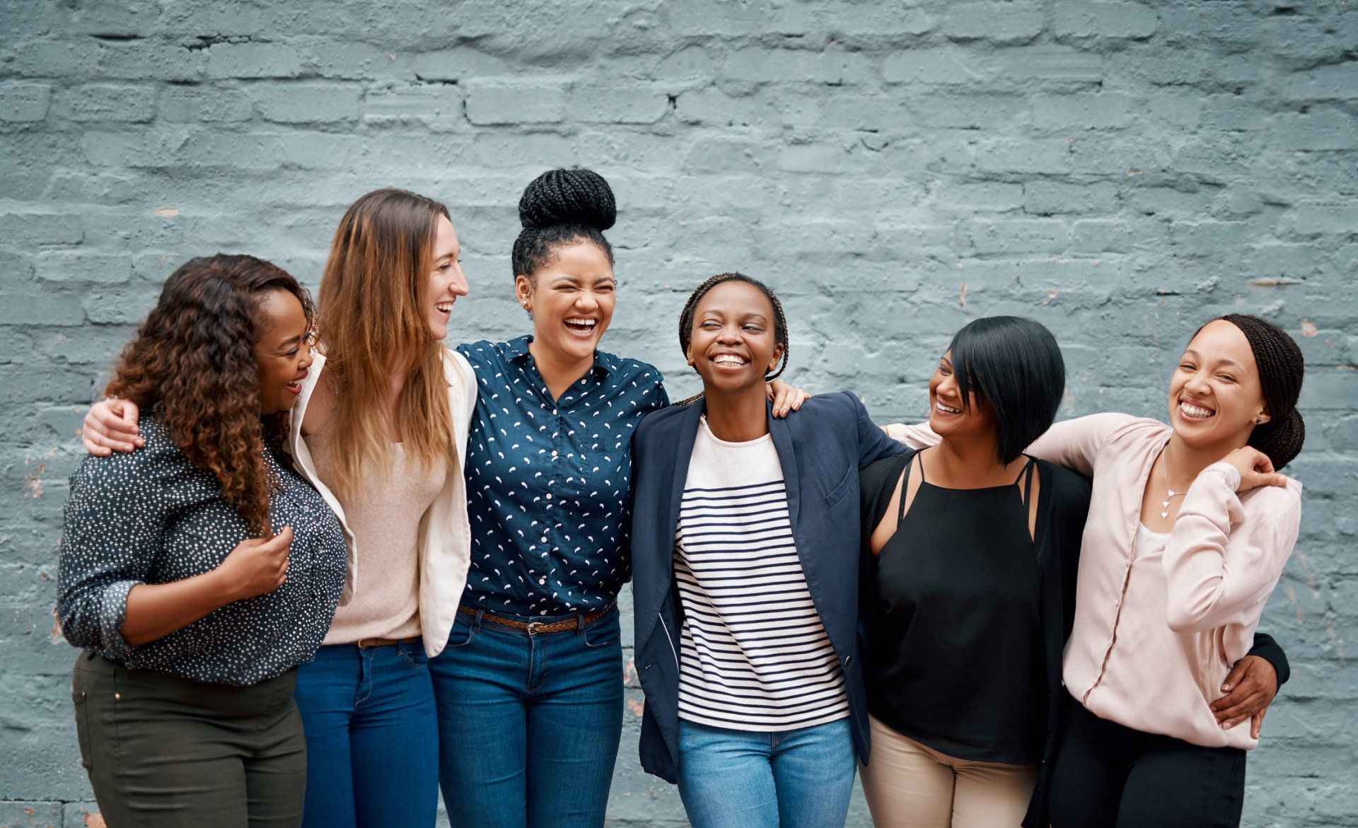 A group of women are standing next to each other in front of a brick wall.