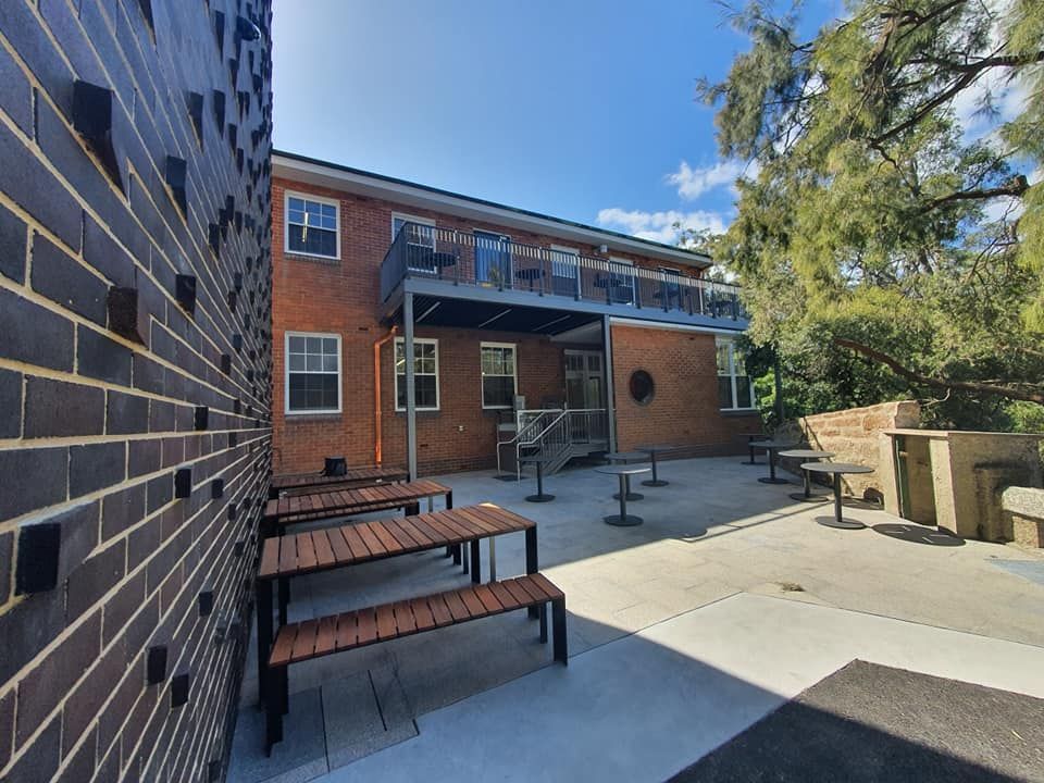 A Brick Building With Wooden Tables and Benches in Front of It — Proweld Steel Fabrication In Southern Highlands, NSW