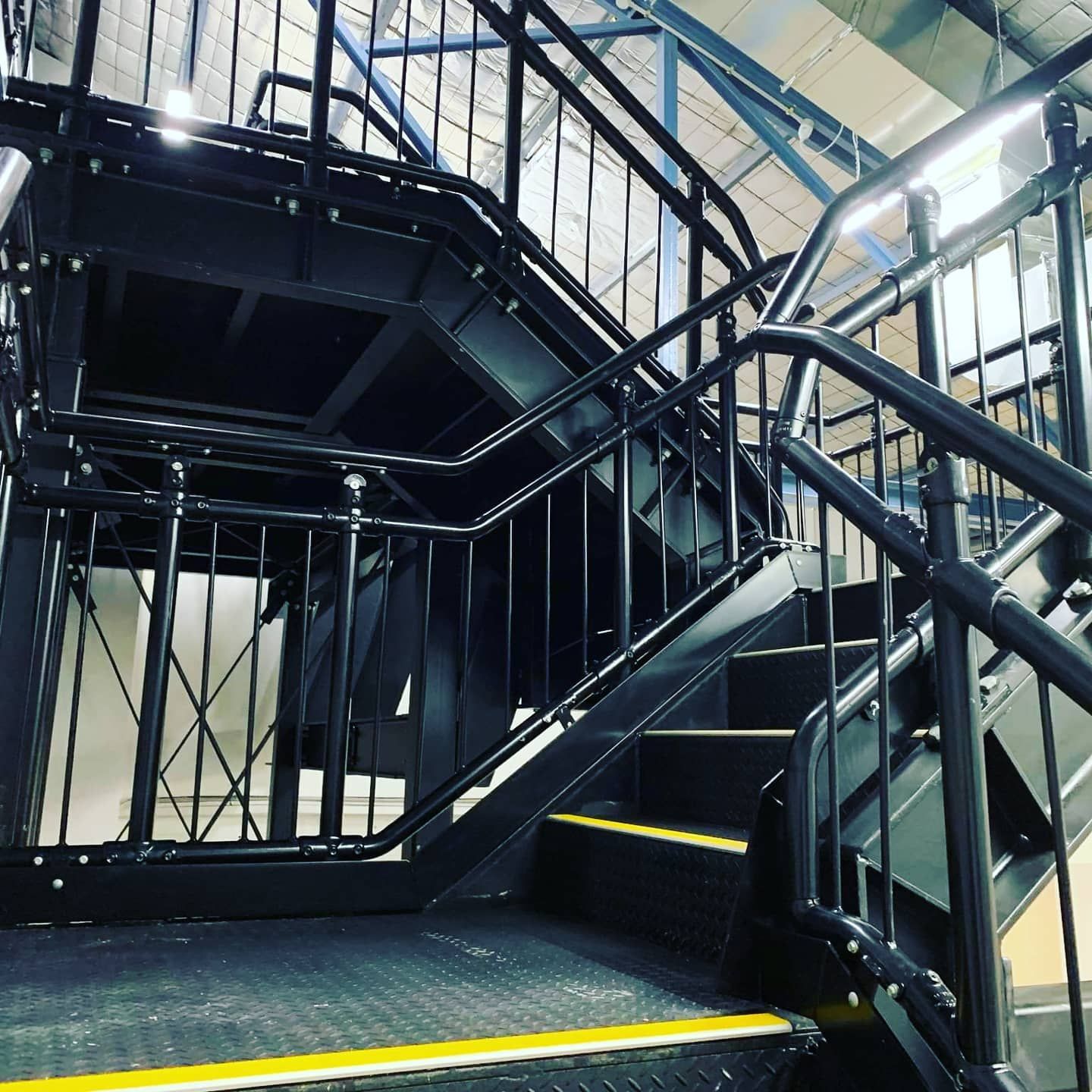 A Black Metal Staircase With a Yellow Stripe on the Bottom Step — Proweld Steel Fabrication In Shellharbour, NSW