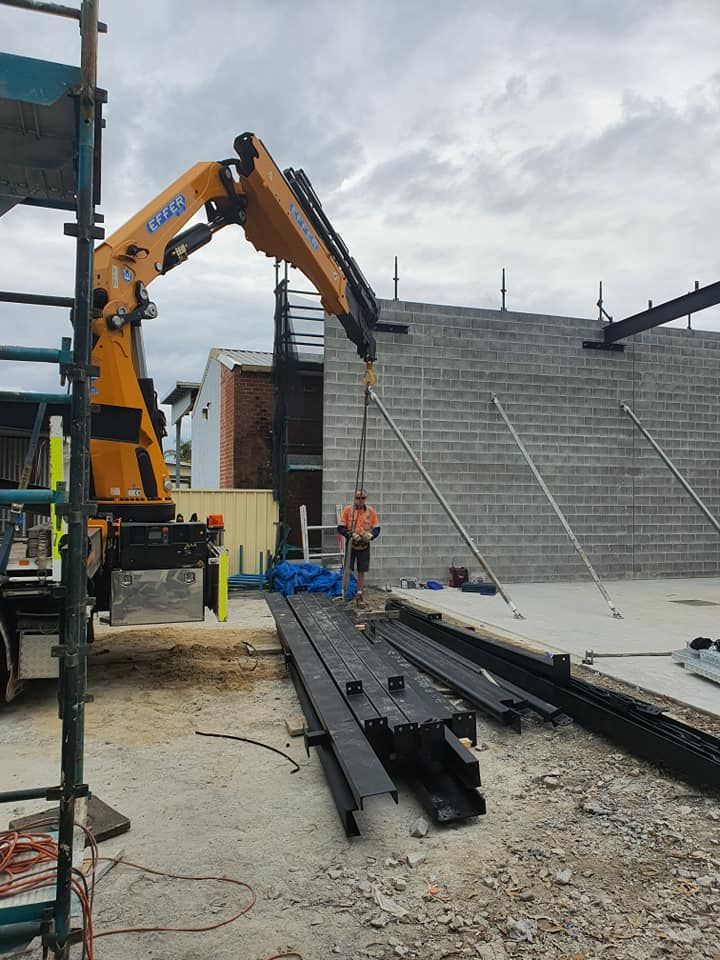 A Crane Lifts Steel Beams at A Construction Site — Proweld Steel Fabrication In Nowra, NSW