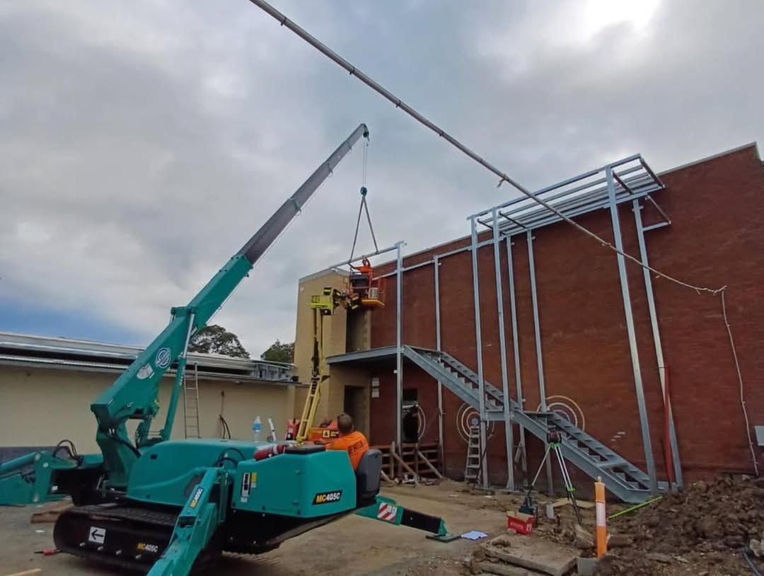 Crane Lifting Object Near New Metal Stairwell on a Brick Building — Proweld Steel Fabrication In Unanderra, NSW