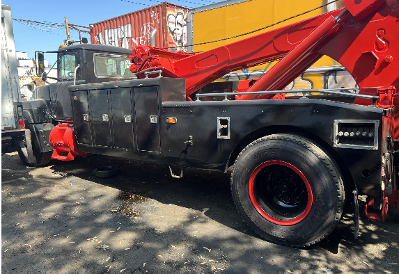 A black and red tow truck is parked in front of a shipping container