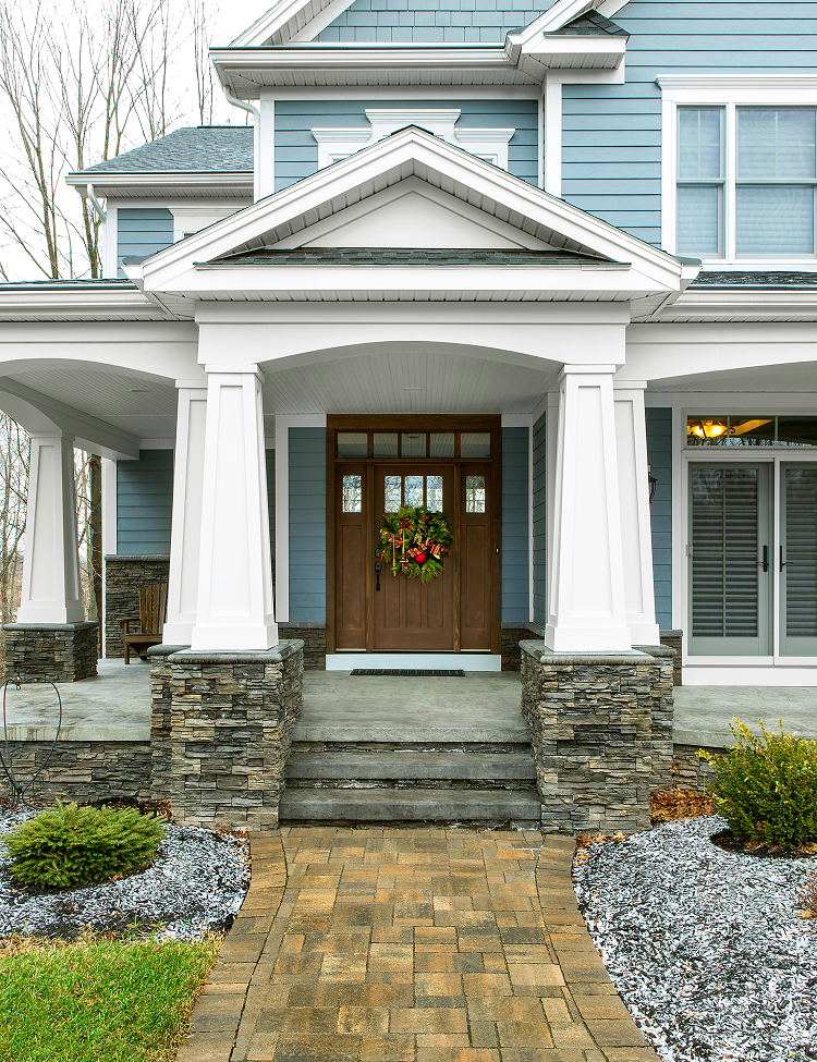 Blue house with stone columns, brown door, and brick pathway leading to the entrance.