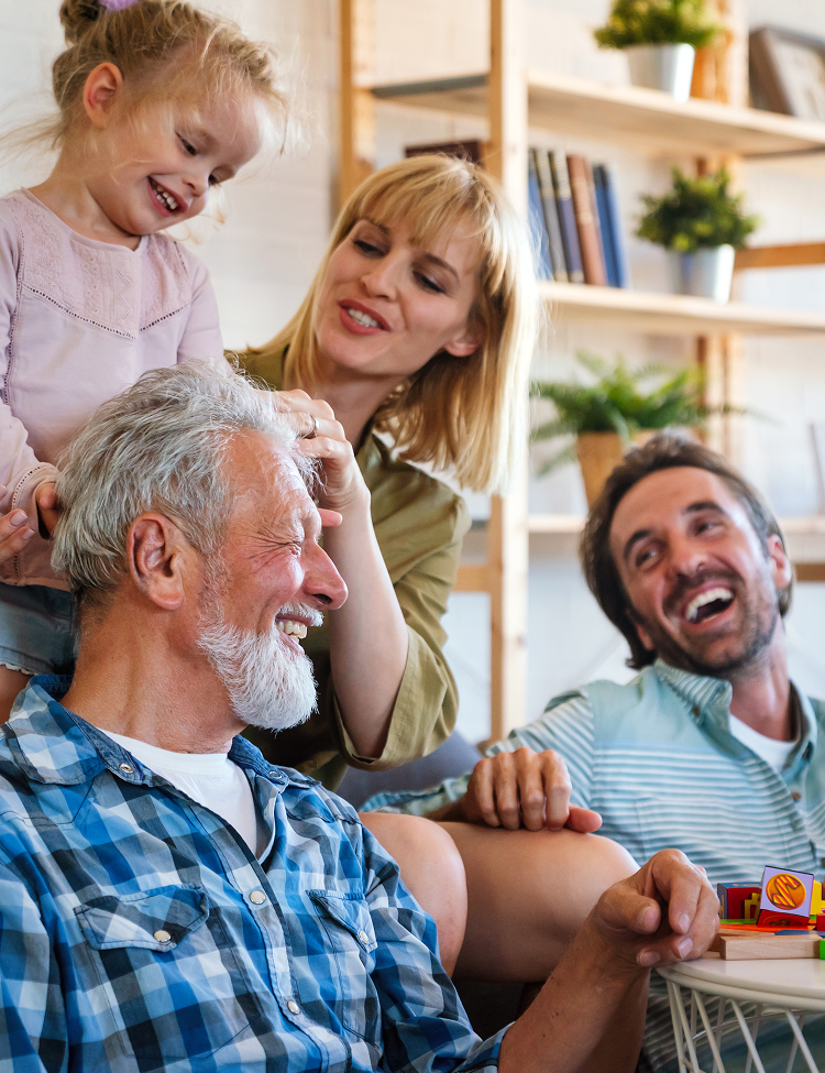 Family smiling together: a grandfather, daughter, granddaughter, and son in a living room.