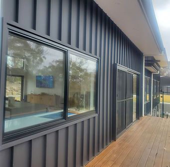 A black house with a lot of windows and a wooden deck.