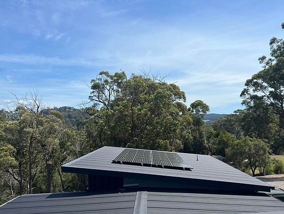 A roof with solar panels on it and trees in the background.