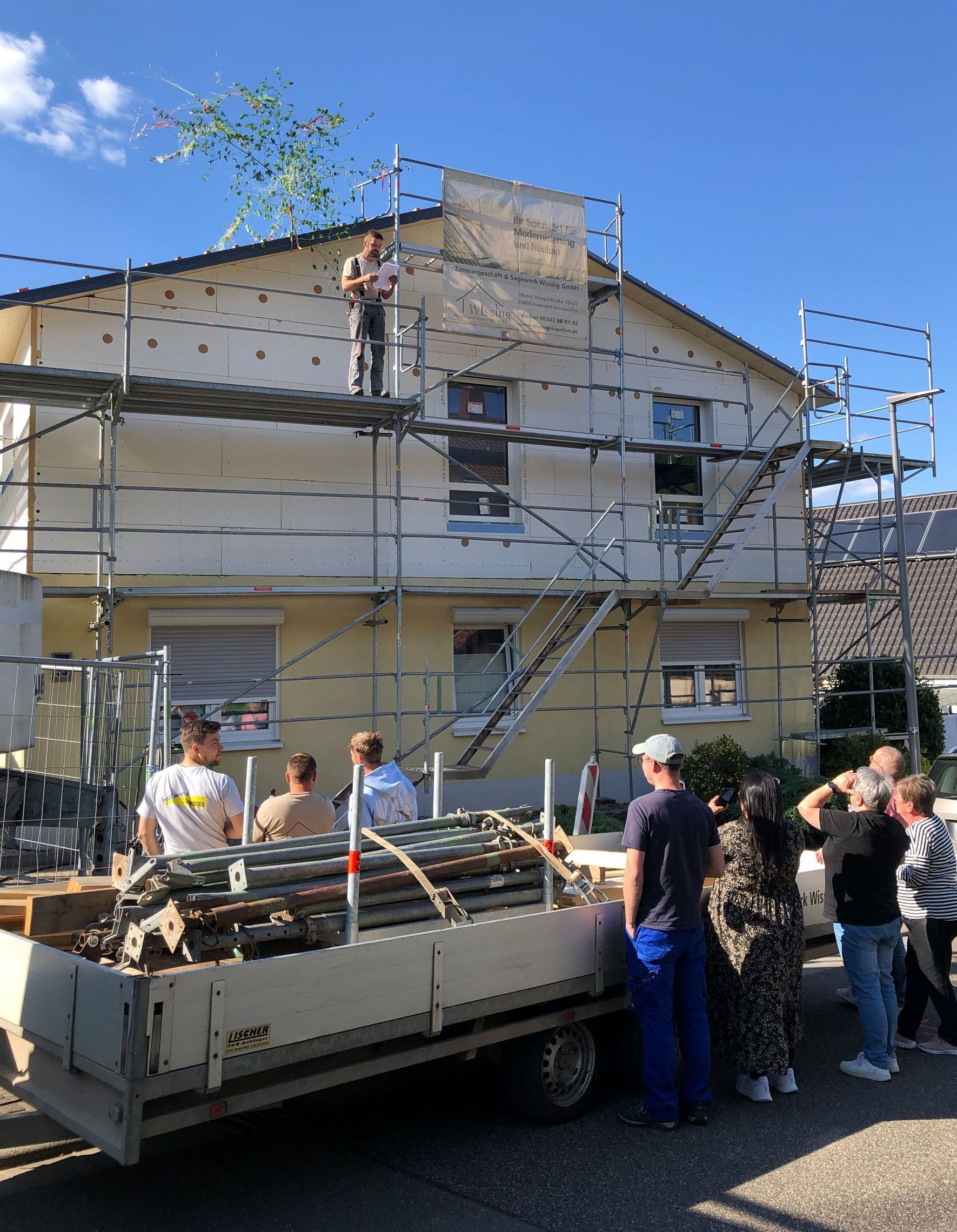 Hier wird Richtfest gefeiert. Der Aufbau steht. Auf dem Gerüst steht ein Zimmermann, der gerade den Richtspruch vorträgt.