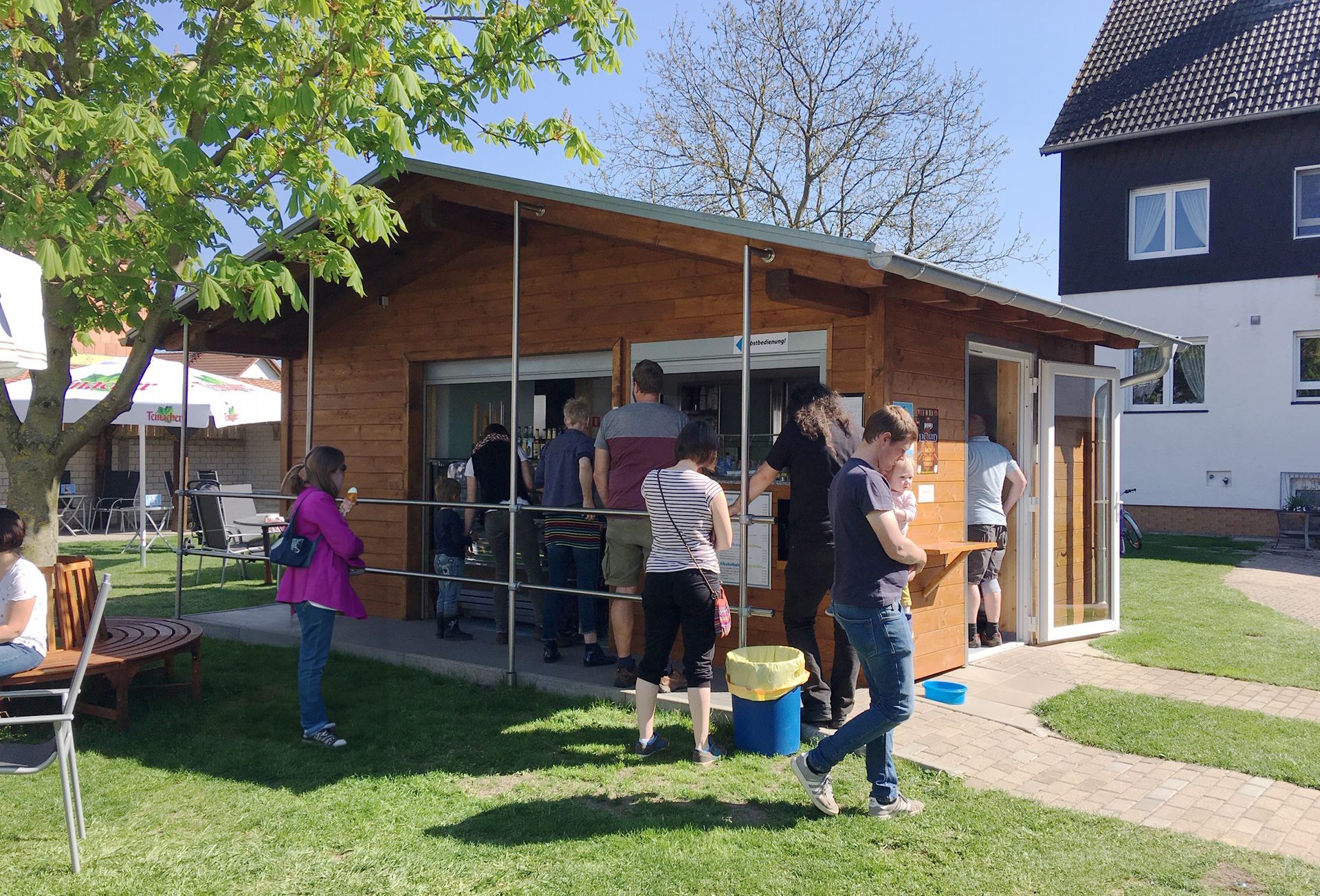 Eine kleine Holzhütte welche als Eisdiele genutzt wird. Ein paar Menschen stehen und sitzen in der Umgebung.