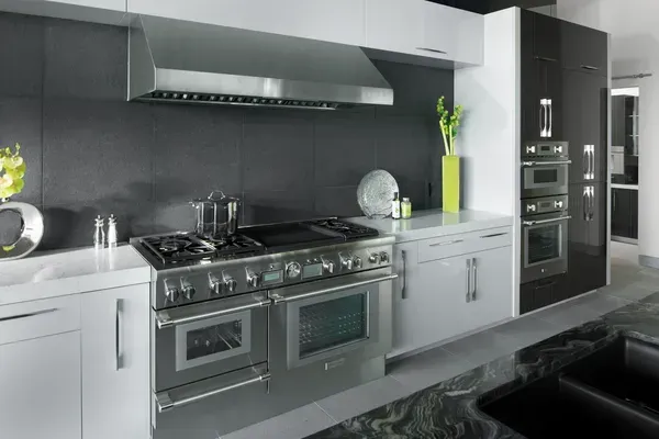 Stainless steel professional kitchen range and hood in modern kitchen with dark gray backsplash.