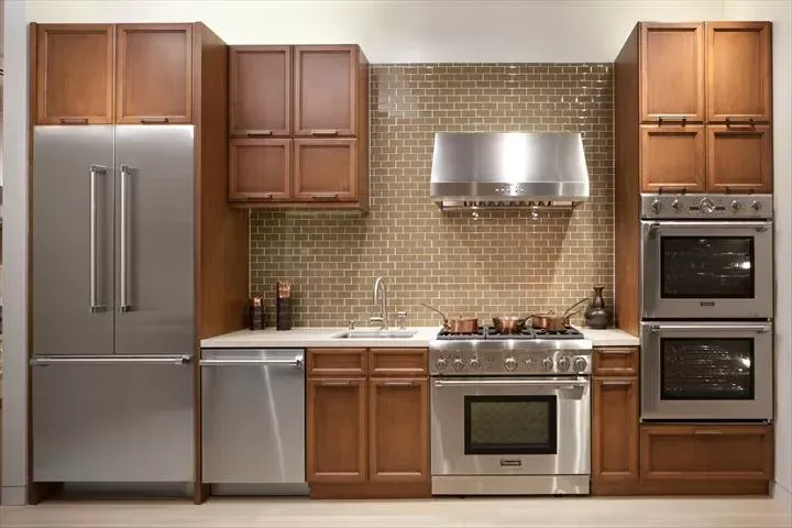 Kitchen with stainless steel appliances, brown cabinets, and tan brick backsplash.