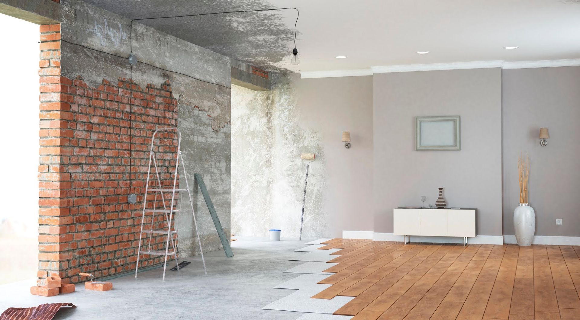 Stanza parzialmente ristrutturata con parete in mattoni a vista, soffitto in cemento e pavimento in legno accanto a un semplice armadio bianco.