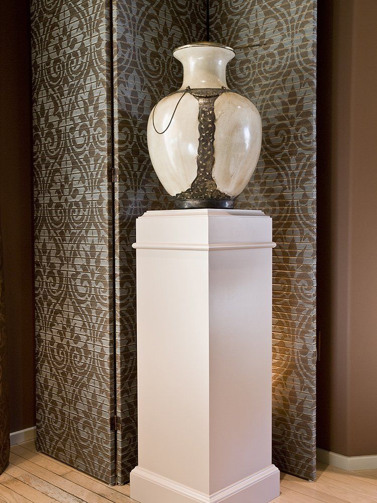 A vase on a pedestal in front of a screen