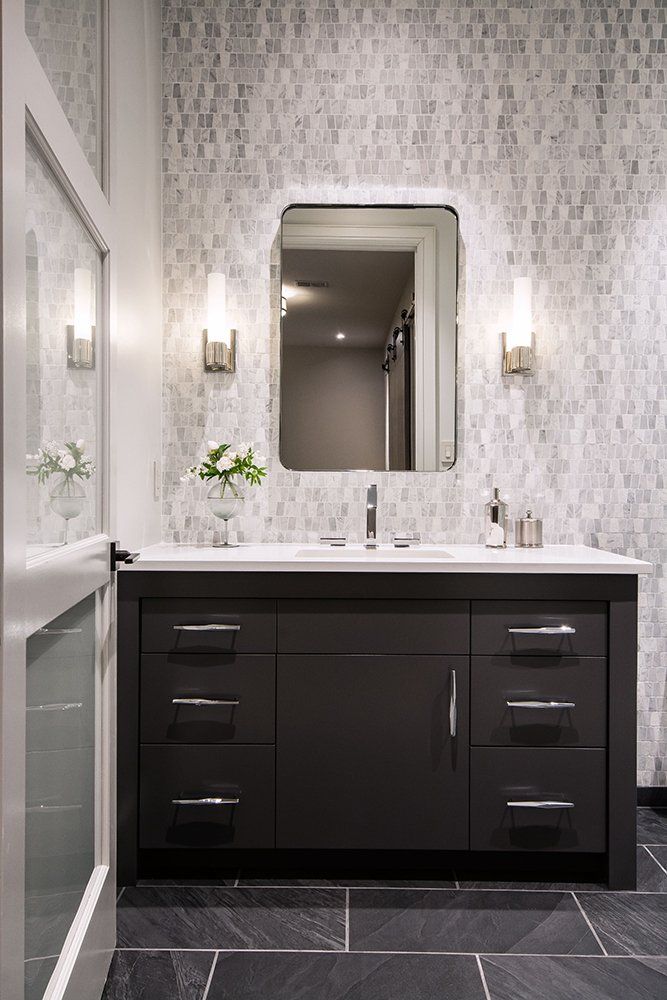 A bathroom with a sink , mirror , and black cabinets.