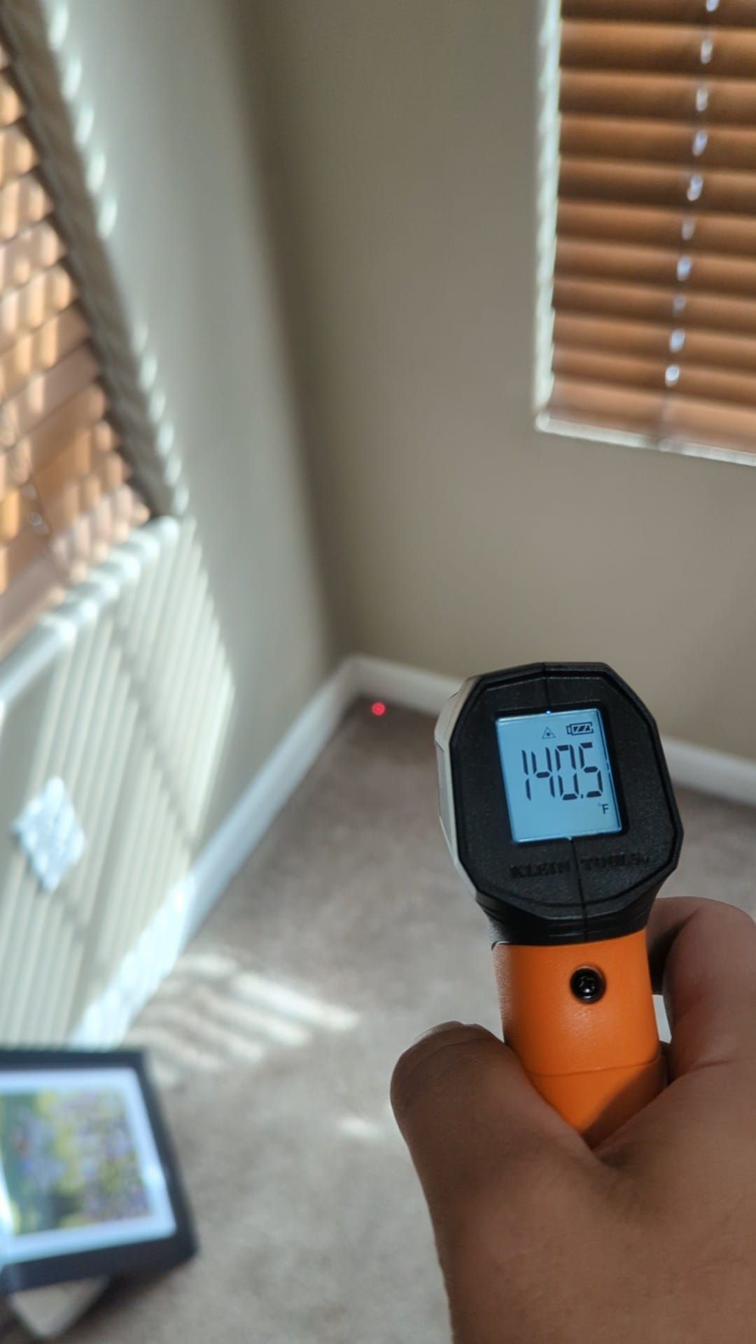 A person is holding a thermometer in a room with blinds.