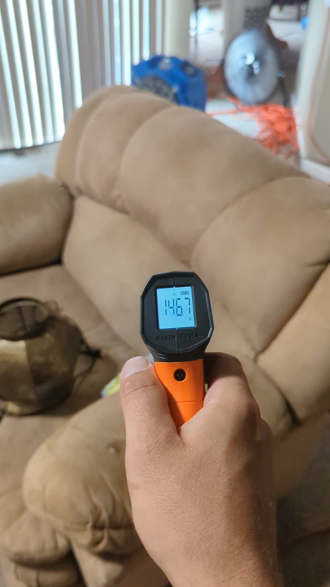 A person is holding a thermometer in front of a couch.