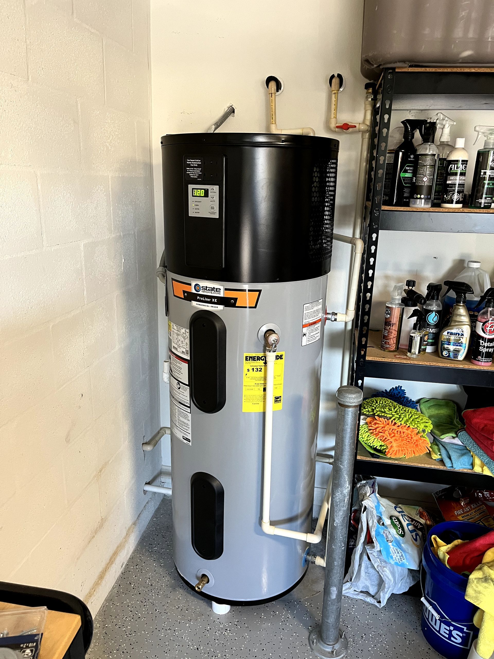 A water heater is sitting in a garage next to a shelf.