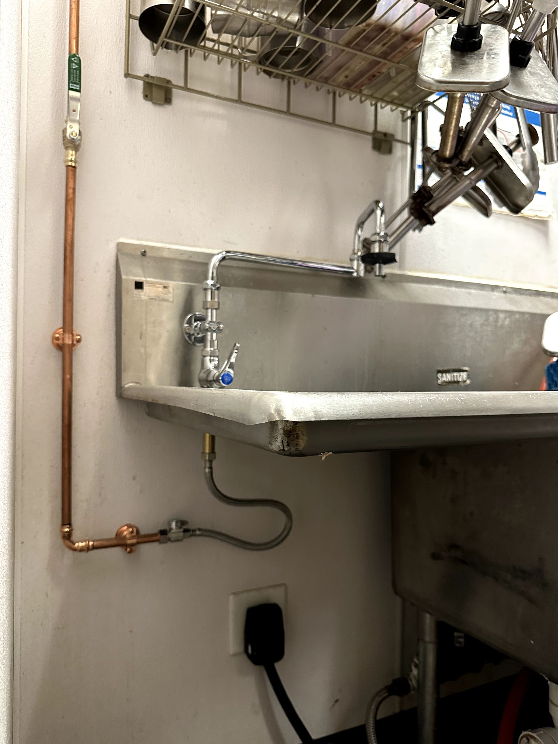 A stainless steel sink with a copper pipe attached to it