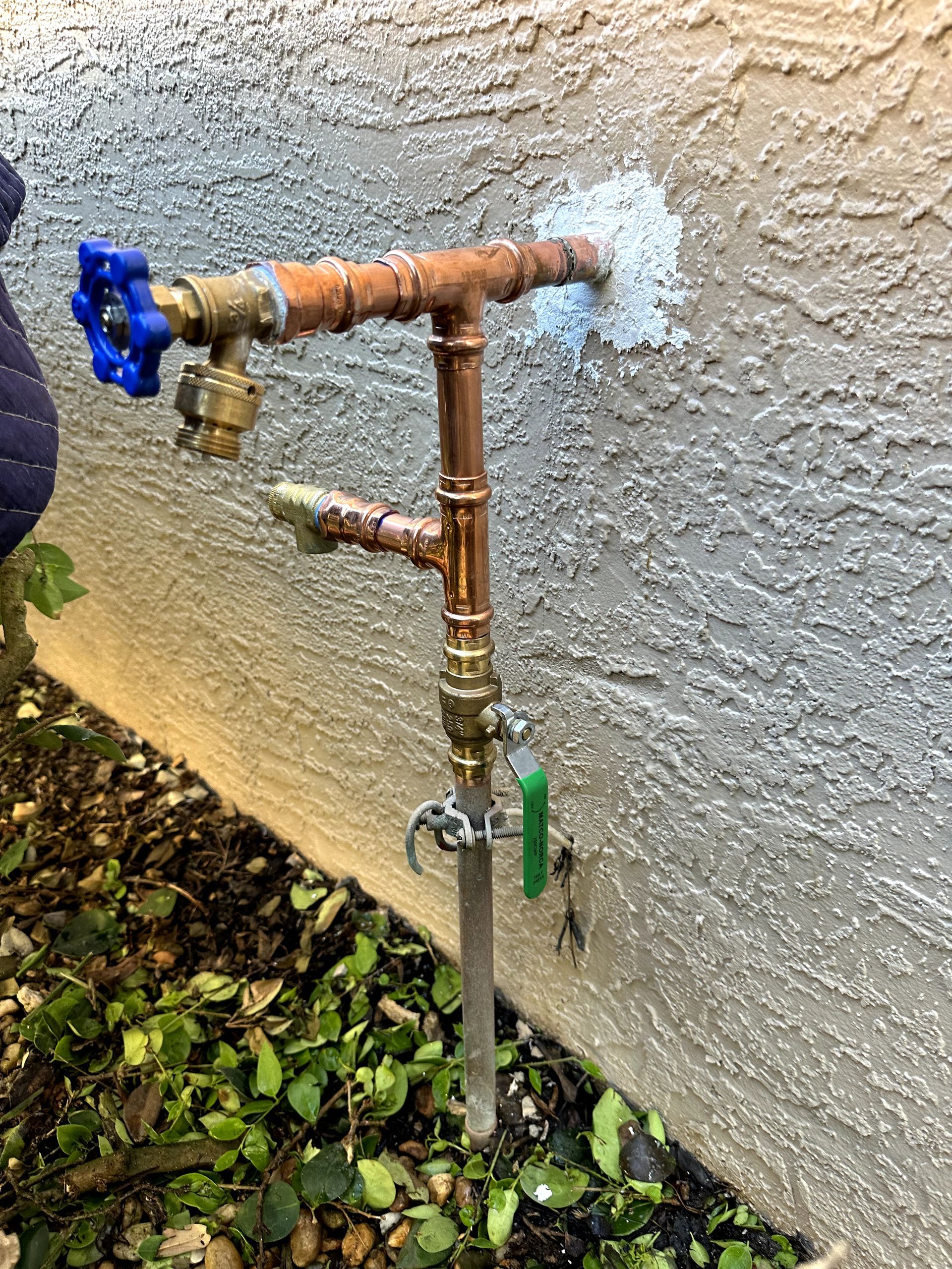 A water faucet is sitting on the side of a building next to a wall.