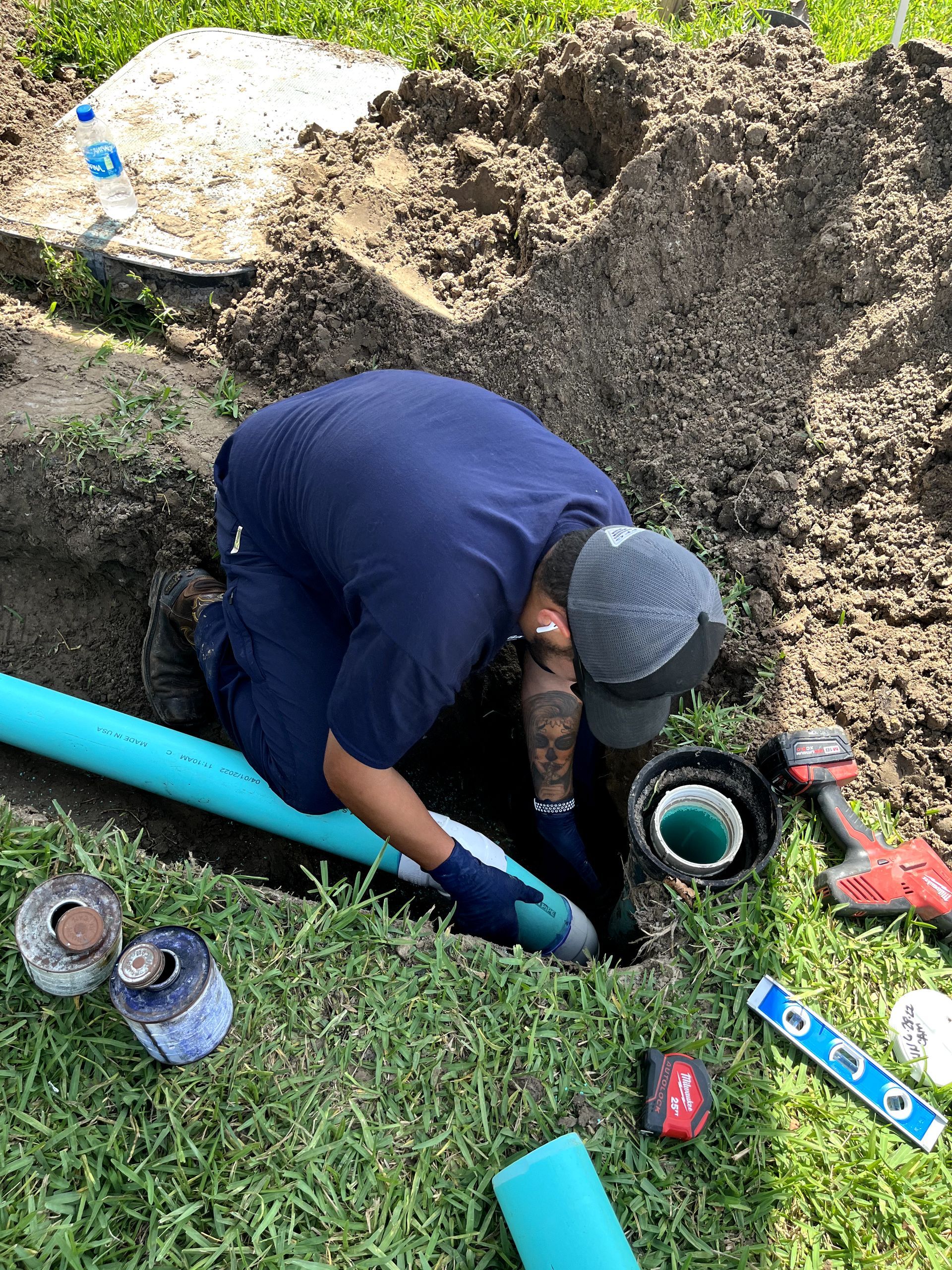 A man is kneeling in the dirt working on a pipe.