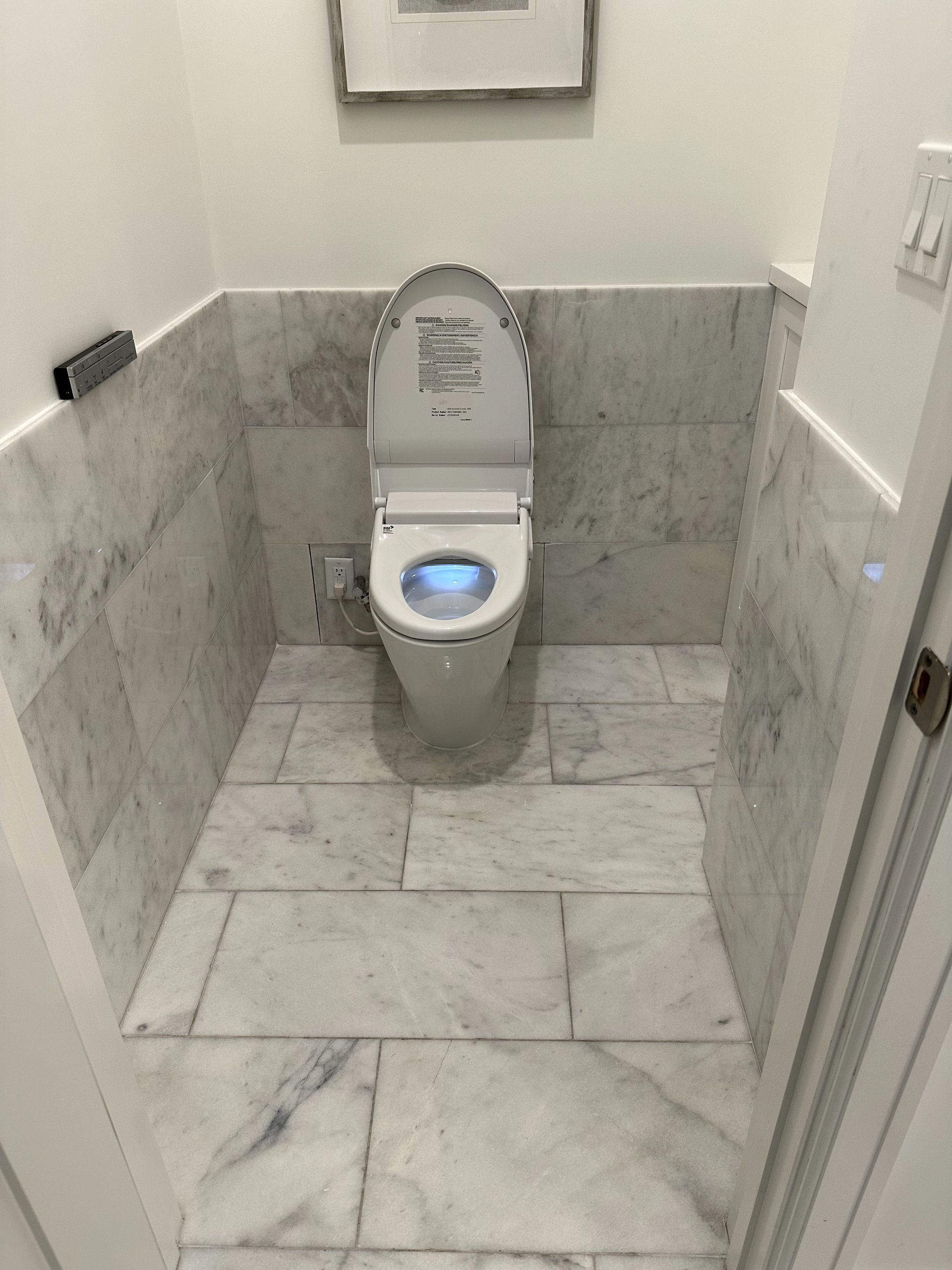 A toilet in a bathroom with marble tiles and a picture on the wall.