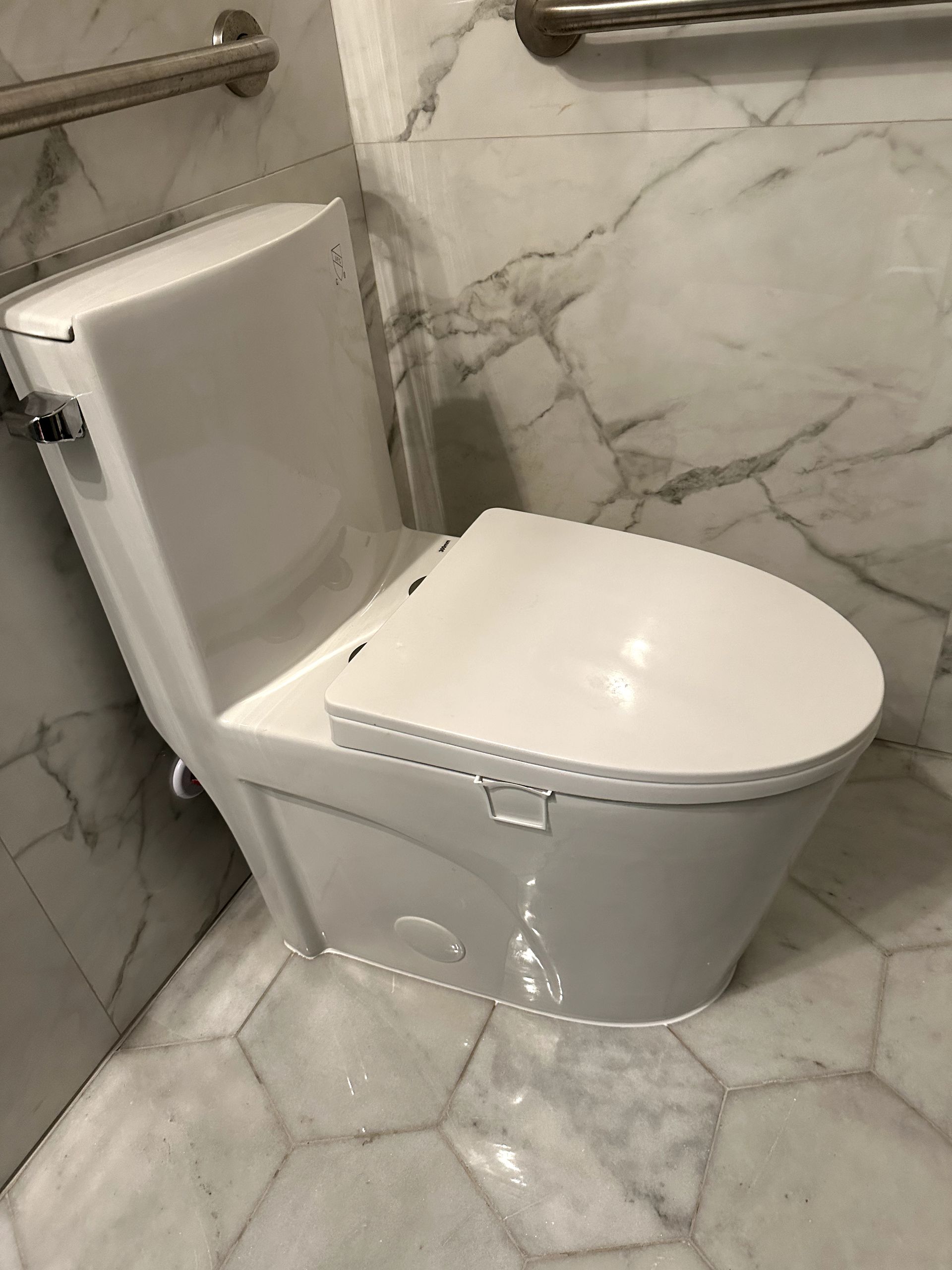A white toilet is sitting in a bathroom next to a marble wall.