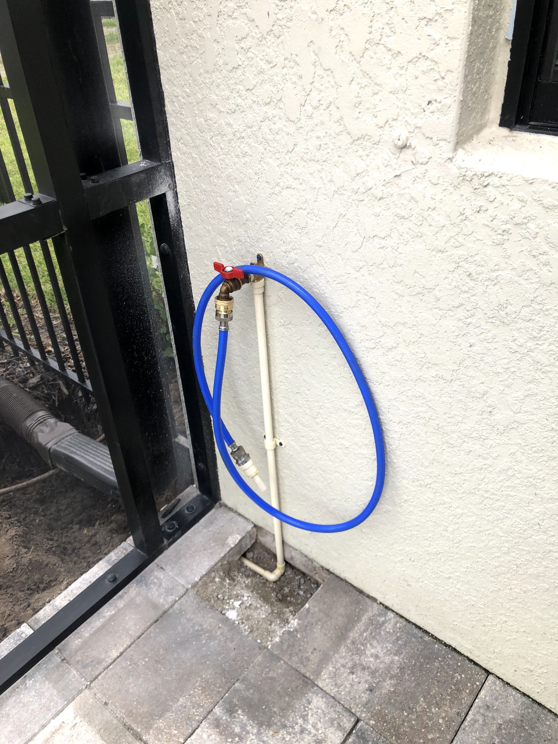 A blue hose is attached to a faucet on the side of a building.