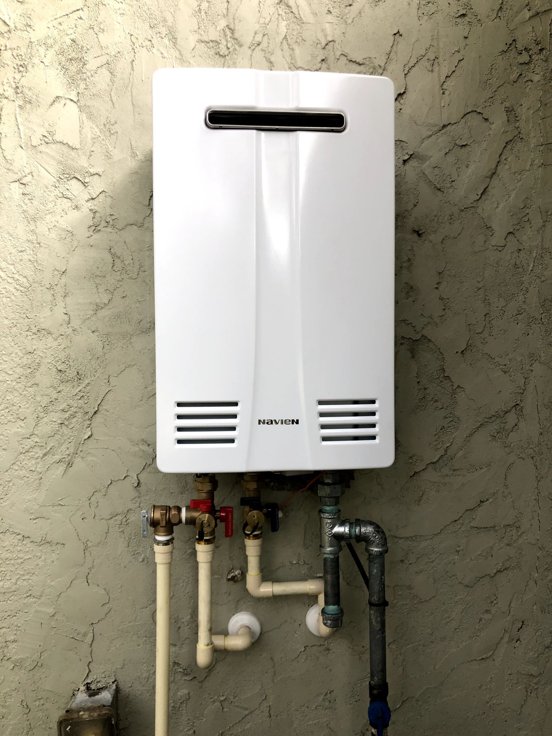 A white water heater is attached to a wall with pipes.
