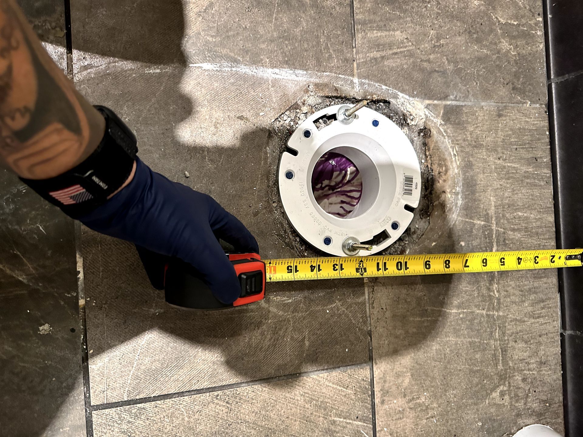 A person is measuring a toilet flange with a tape measure.