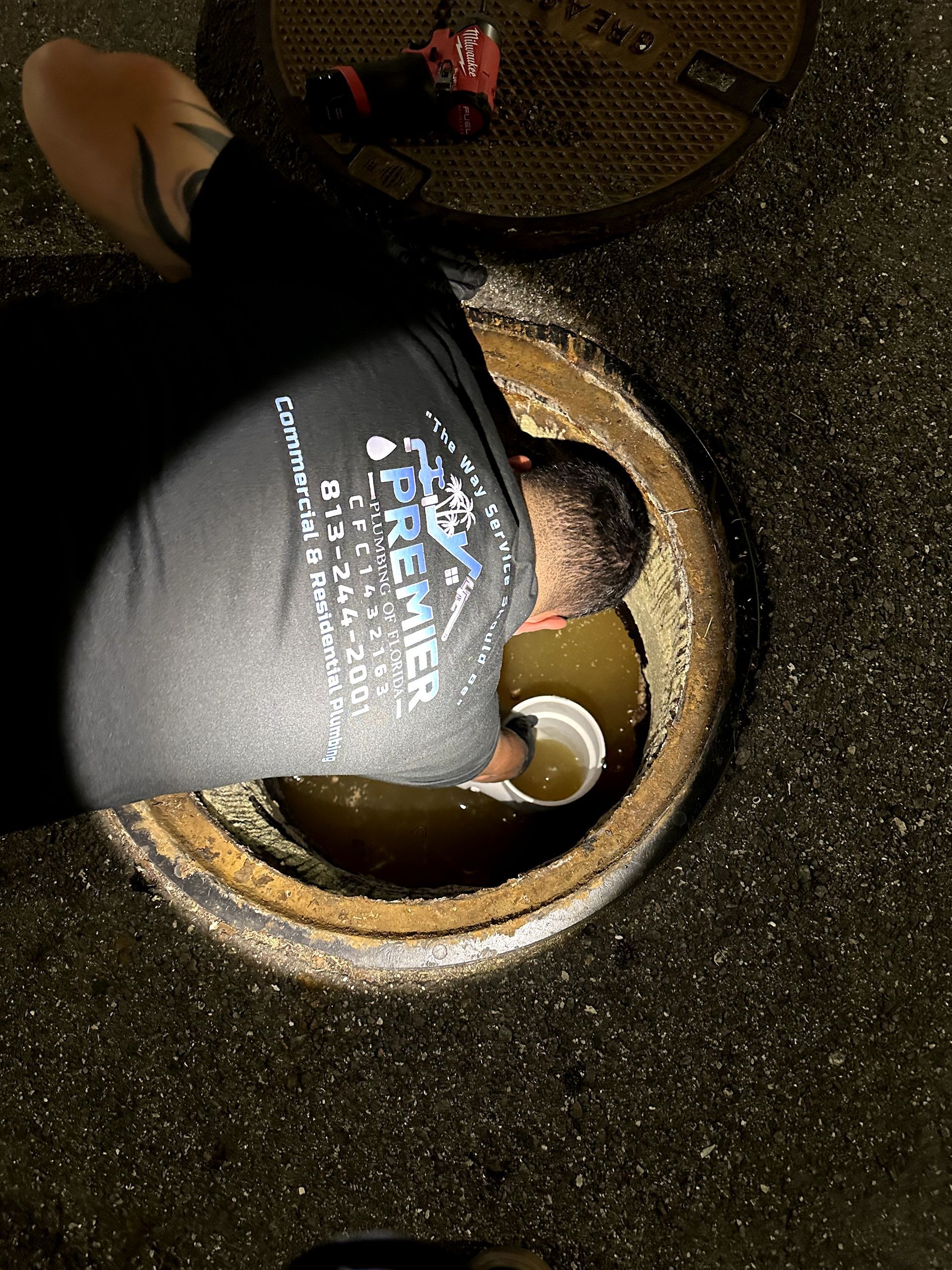 A man in a black shirt is looking into a manhole cover.