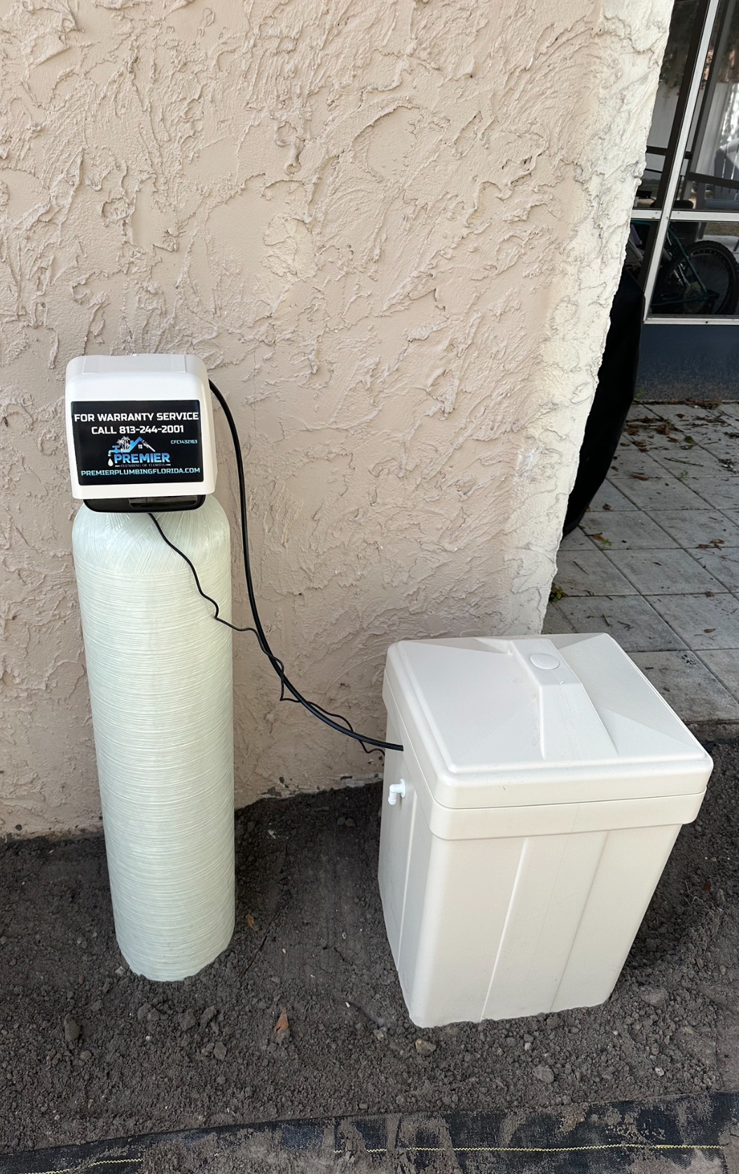 A water softener is sitting on the sidewalk next to a wall.