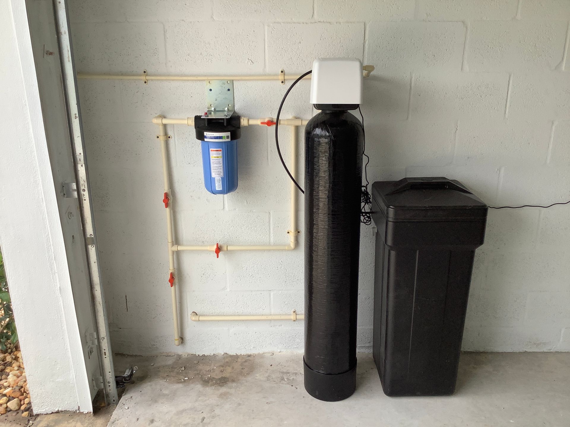 A water filter is sitting next to a trash can in a garage.