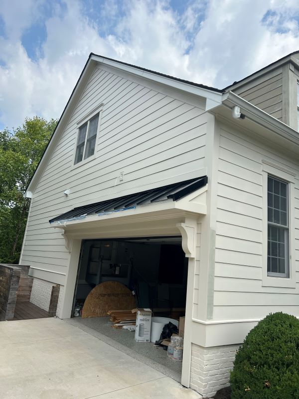 White house with open garage, black roof trim, and small window.