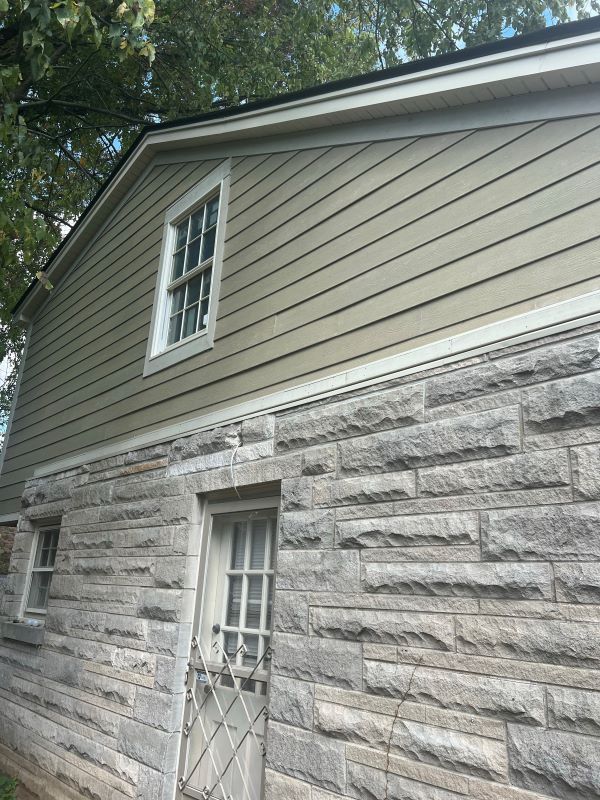 Exterior of a building with gray stone and green siding, with a window in each section.