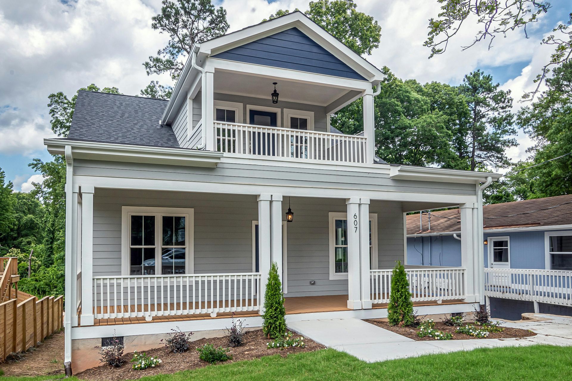 A newly built, gray house with white trim and a covered porch, set on a brown dirt lot.