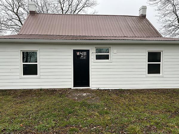 White house with brown roof and black door, set against a gray sky. Two chimneys flank the roof.