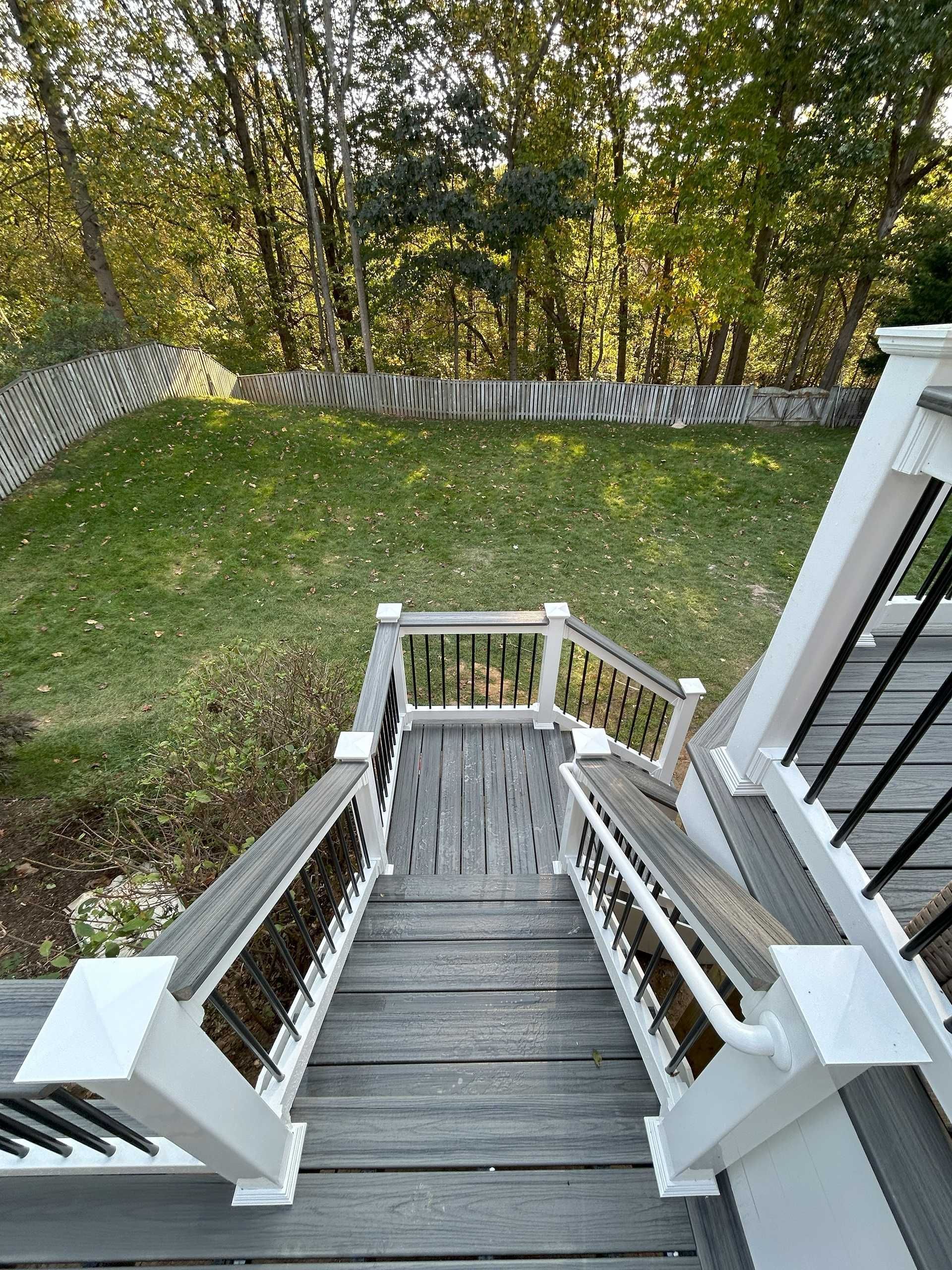 Wooden deck stairs leading down to a grassy yard with trees in the background.