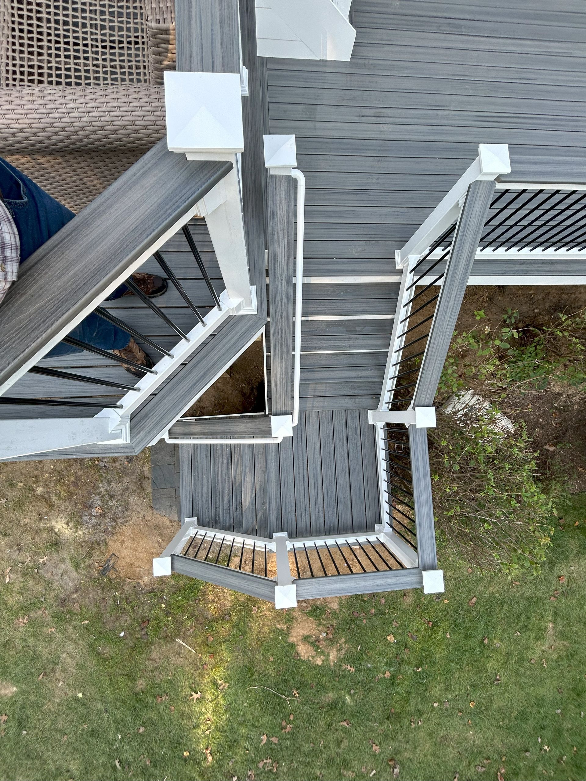 Overhead view of a composite deck with stairs and black railings, surrounded by green grass.