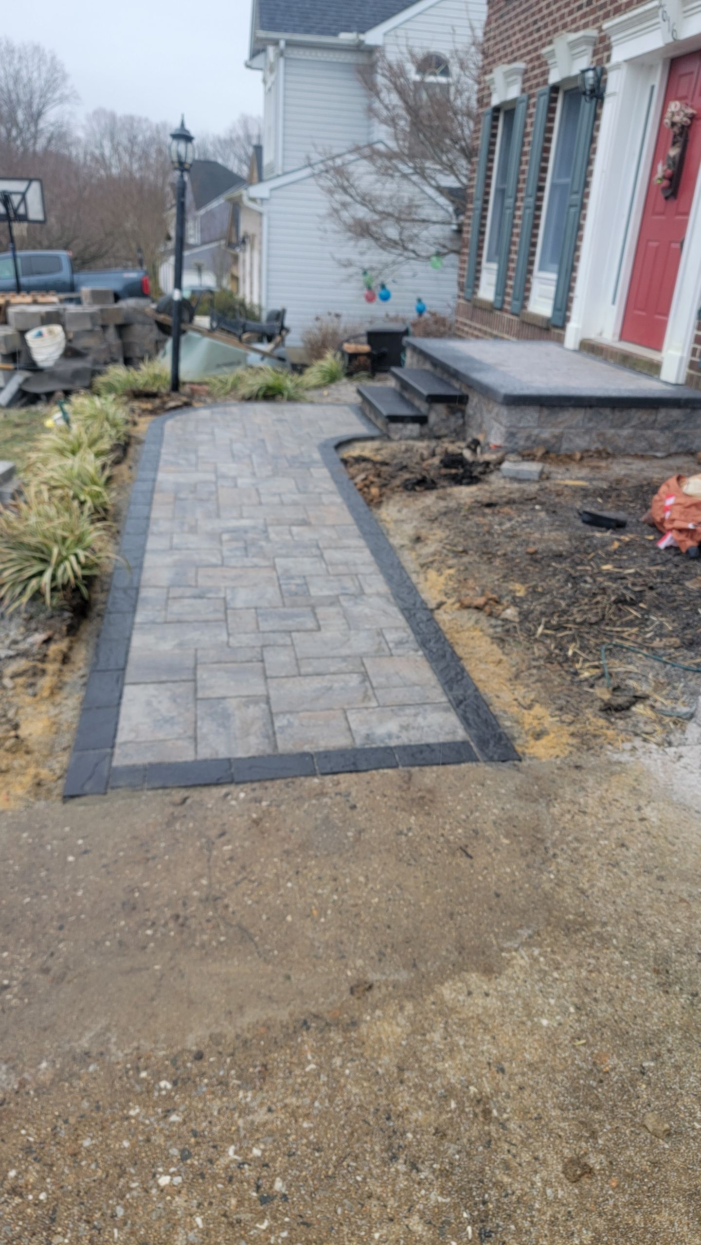 Stone walkway leading to a house with brick facade. Gray pavers bordered with dark stone, overcast day.