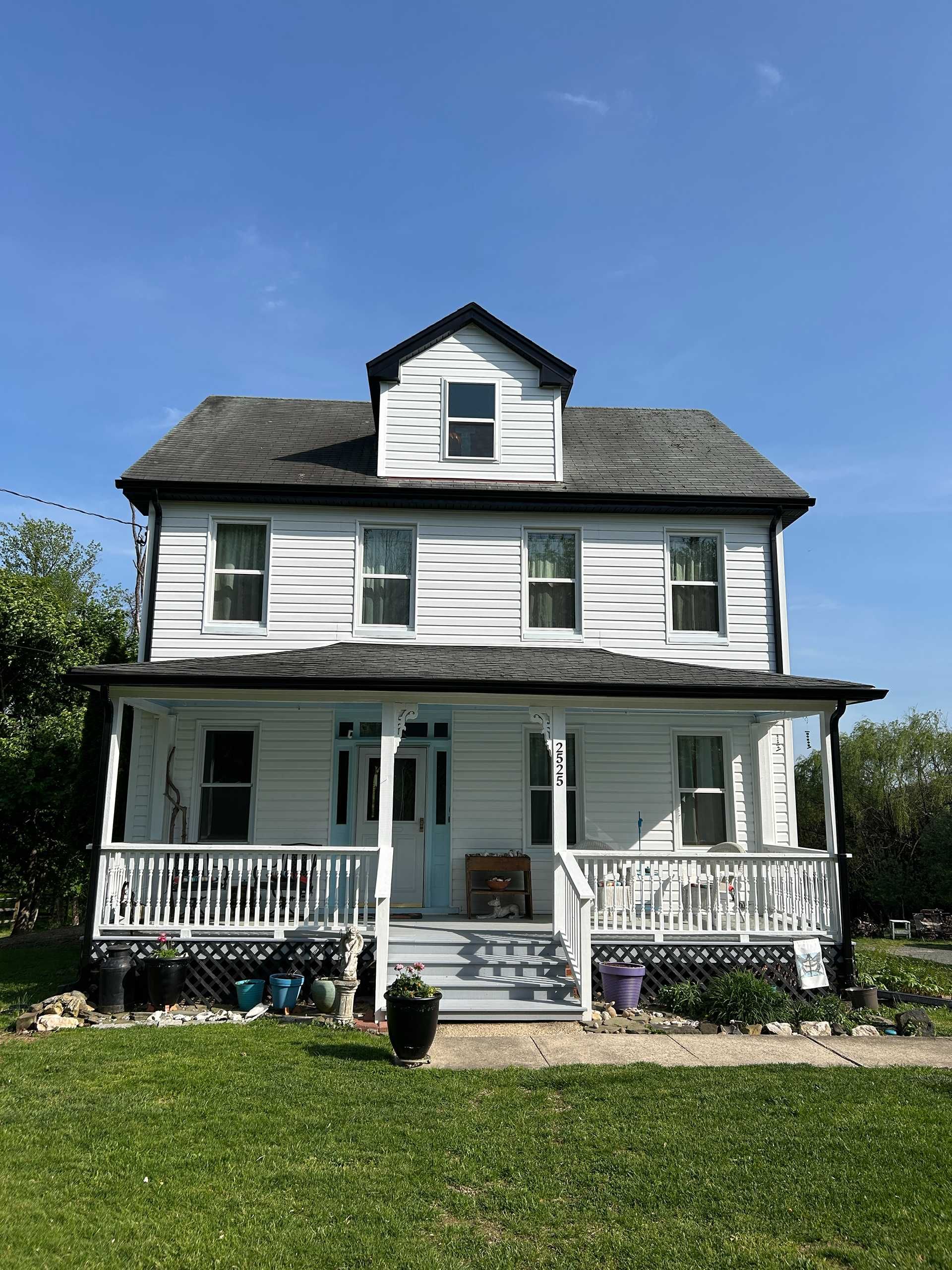 White two-story house with a porch and dormer under a bright blue sky.