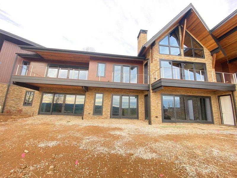 Two-story modern home with brick and wood siding, large windows, and an outdoor deck under a cloudy sky.