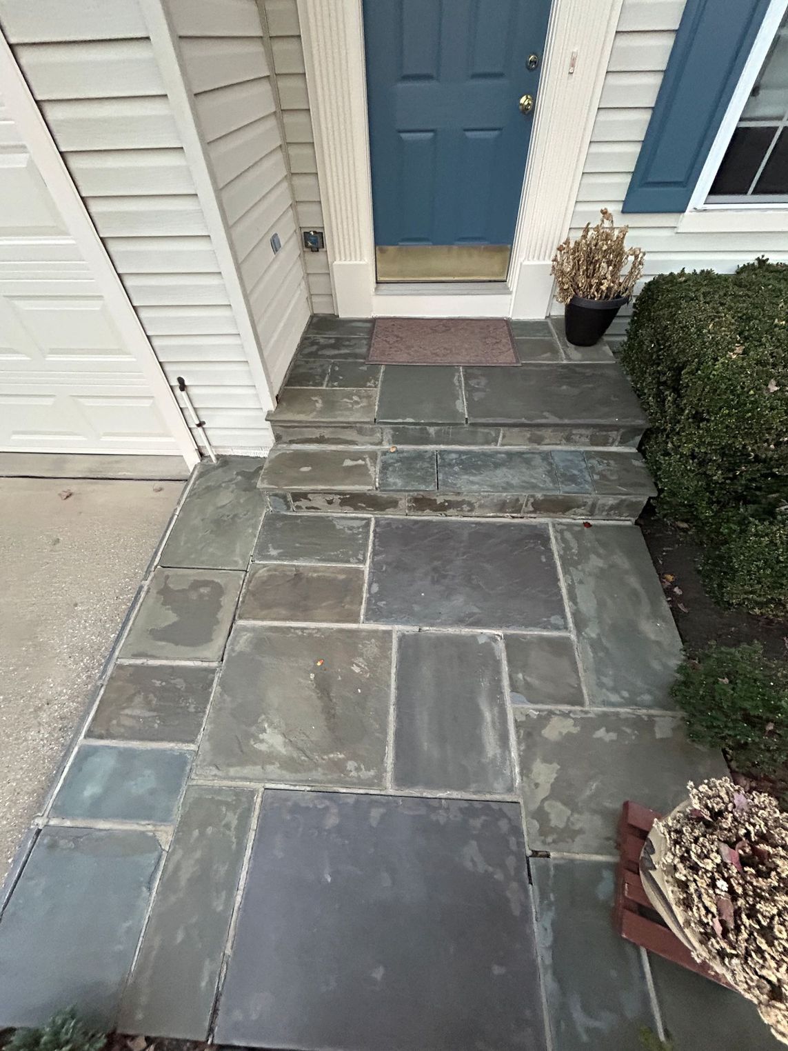 Stone walkway and steps leading to a blue front door with a doormat; potted plant on the right.