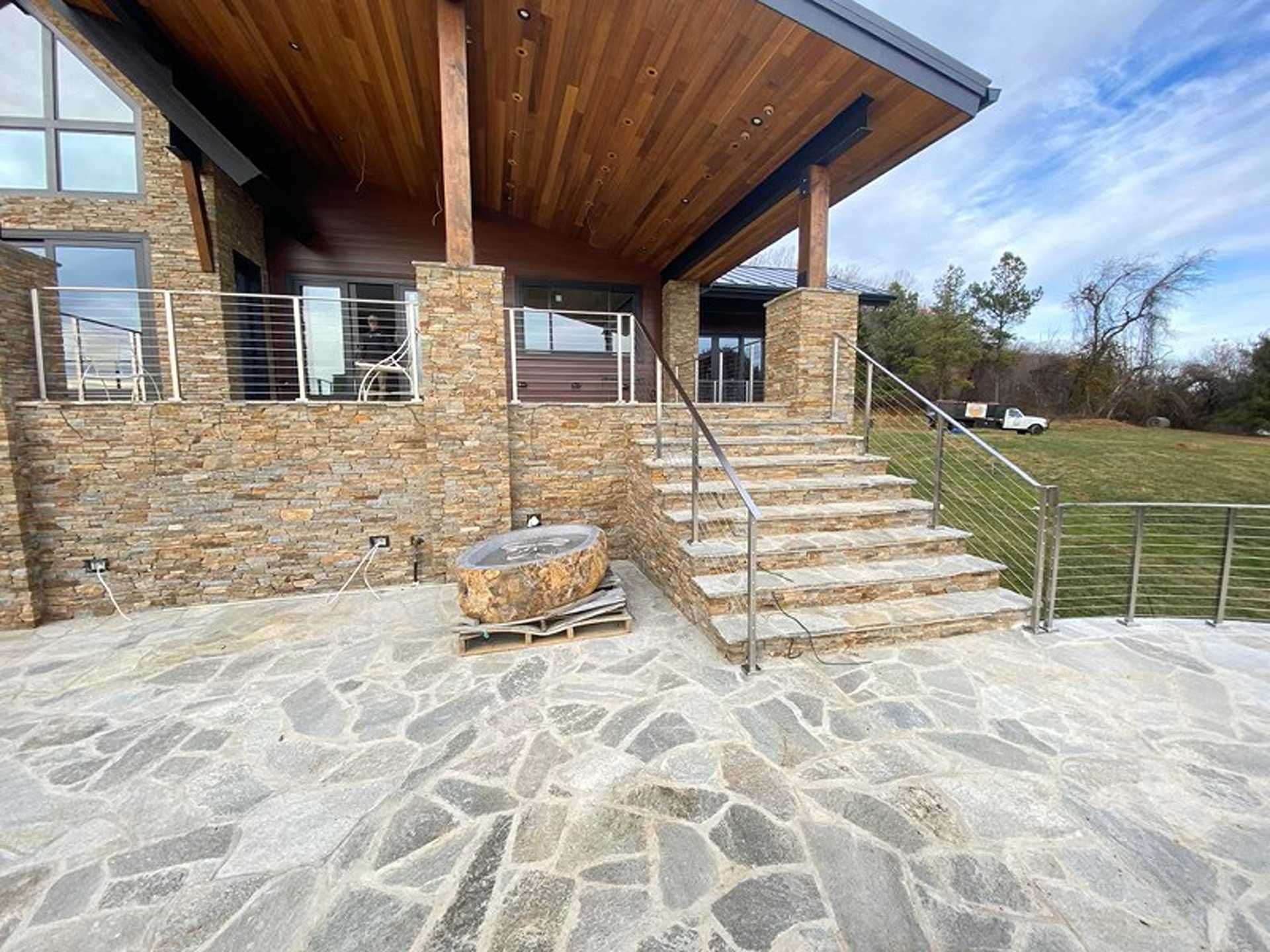 Stone home exterior with steps, stainless steel railings, stone patio, and grassy yard.